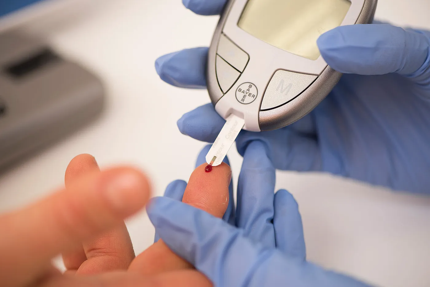 Fachpersonal in Handschuhen misst mit einem Messgerät den Blutzucker aus einem Tropfen Blut am Finger
