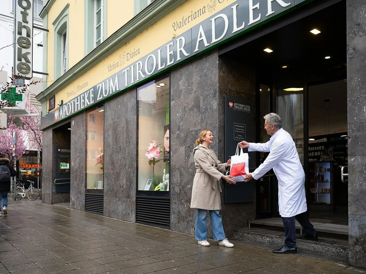 Ein Apotheker überreicht einer Kundin vor dem Eingang der Apotheke ein Sackerl mit Medikamenten
